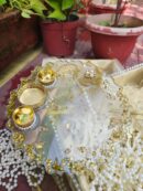 Handcrafted clear resin pooja thali embedded with gold flakes, featuring pearl flower motif, silver leaf filigree, and three golden diya holders.