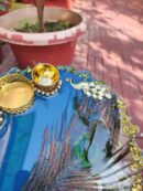 Handcrafted royal blue resin pooja thali featuring peacock feather, Kundan peacock embellishments, and golden diya holders for festive gifting.