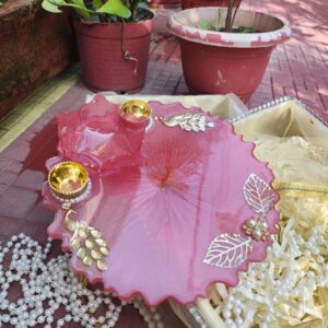 Handcrafted rose pink resin pooja thali featuring 3D lotus bowl, golden leaf filigree, Kundan peacock motifs, and pearl-trimmed diya holders.