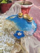Handcrafted ocean blue resin pooja thali featuring blue flower embellishment, golden branch filigree, Kundan peacocks, and built-in golden diya holders.